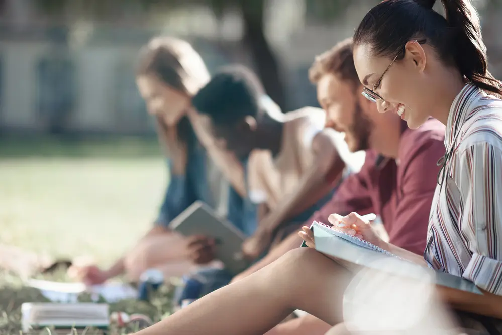 Diverse college students study outside on a lawn.