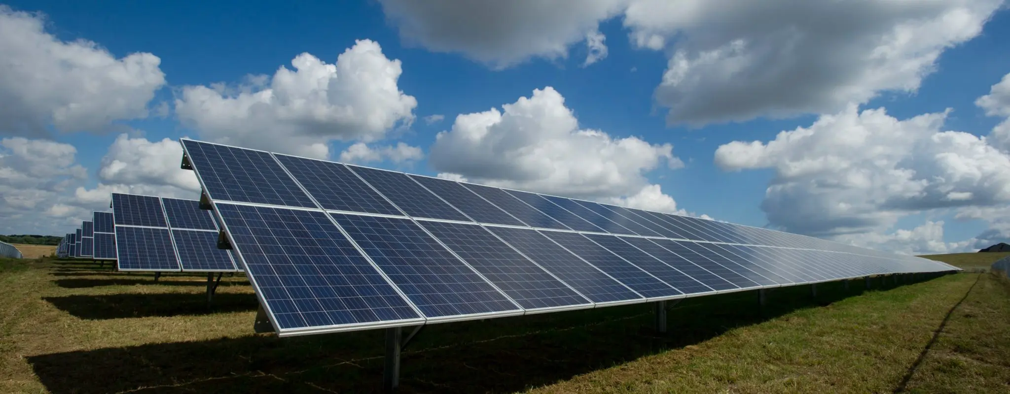 Image of multiple solar panels beneath a shining sun in a grassy field.