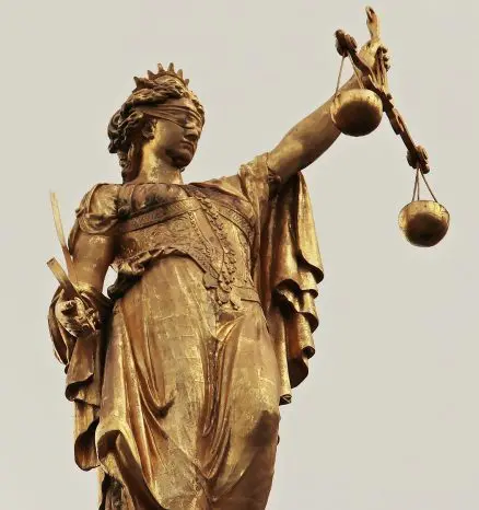 Close-up of golden statue depicting blindfolded Lady Justice with the scales of justice in one hand a sword in another.
