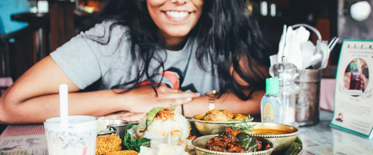 female college student gazes at bowls of side dishes while leaning on restaurant table