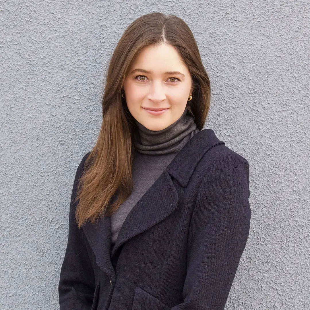 A woman in a gray turtleneck and black coat poses for a headshot