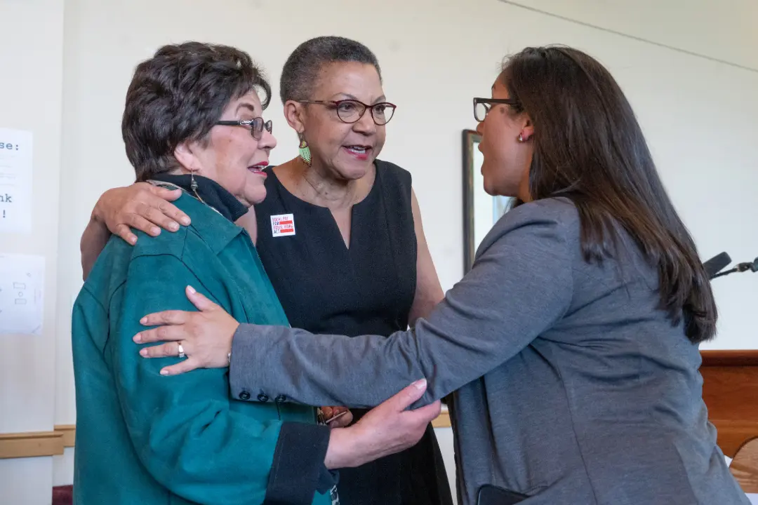 Three professional woman speak closely while embracing