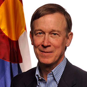 a man in a black blazer poses for a headshot standing in front of the colorado flag