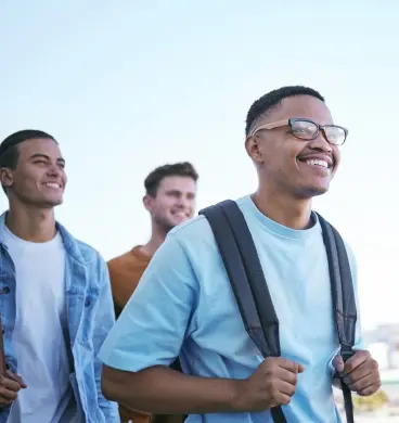 Group of male college students smile. The one in the front carries a backpack.