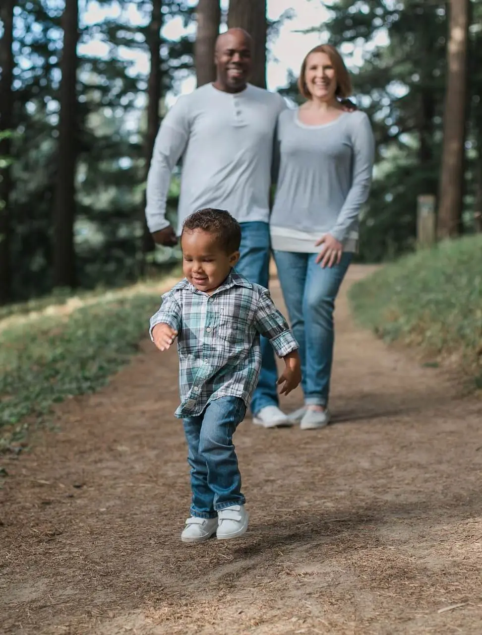 toddler runs ahead as multiracial family walk along hiking trail