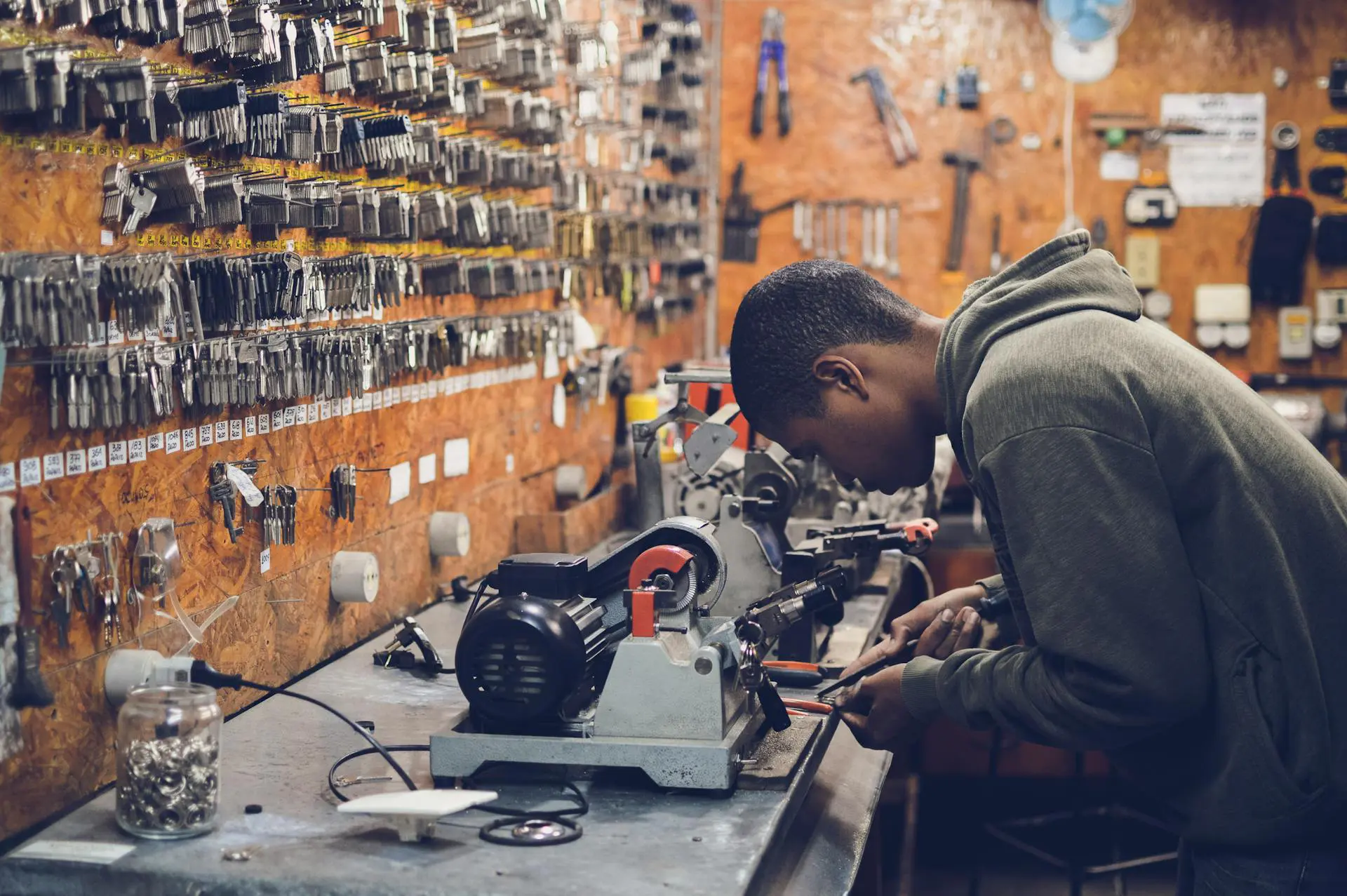 A teenager works on machine in a skilled trade workshop with a wall of keys