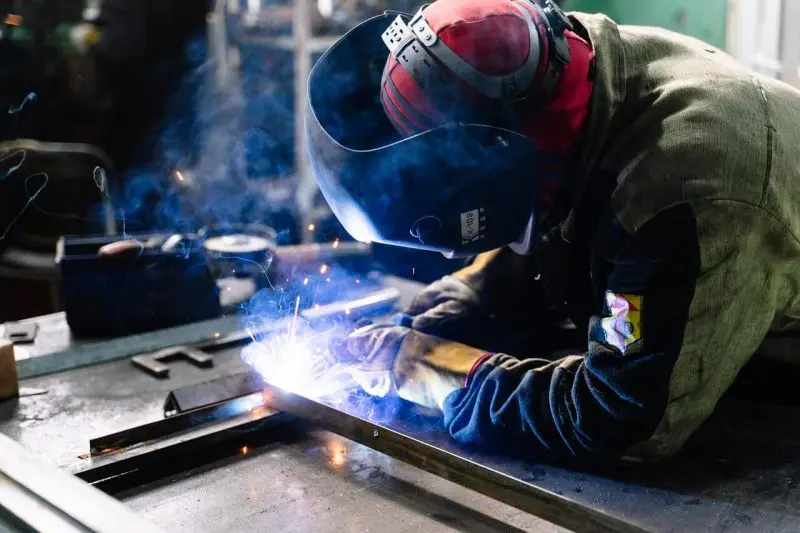 Cose-up shot of a welder at work wearing a respirator, mask, and other protective equipment while sparks fly.