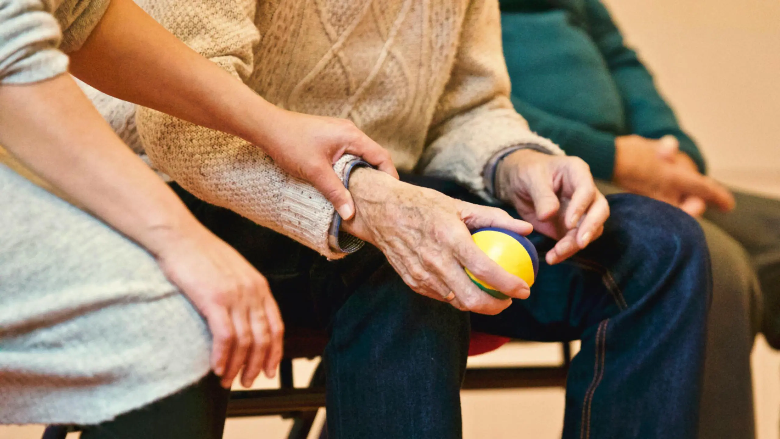 health care worker places their hand on the arm of an elderly person holding a stress ball