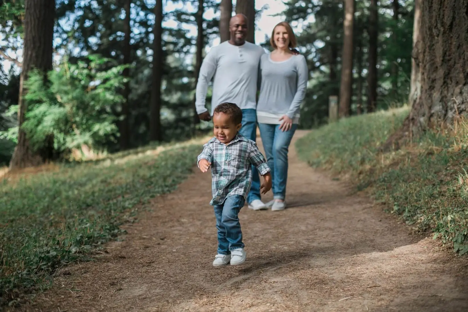 toddler runs ahead as multiracial family walk along hiking trail