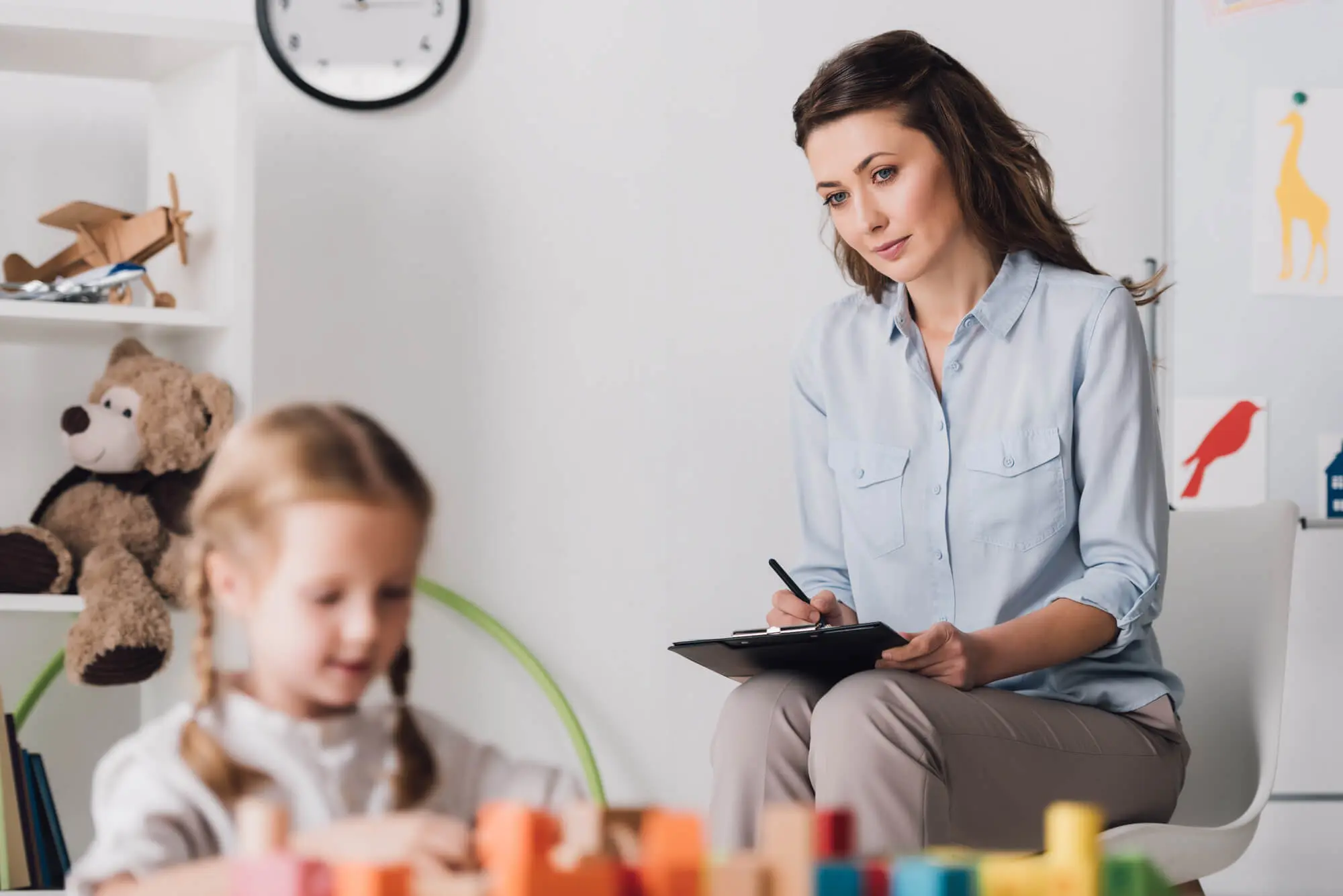 female adult with clipboard observes female child playing with toys