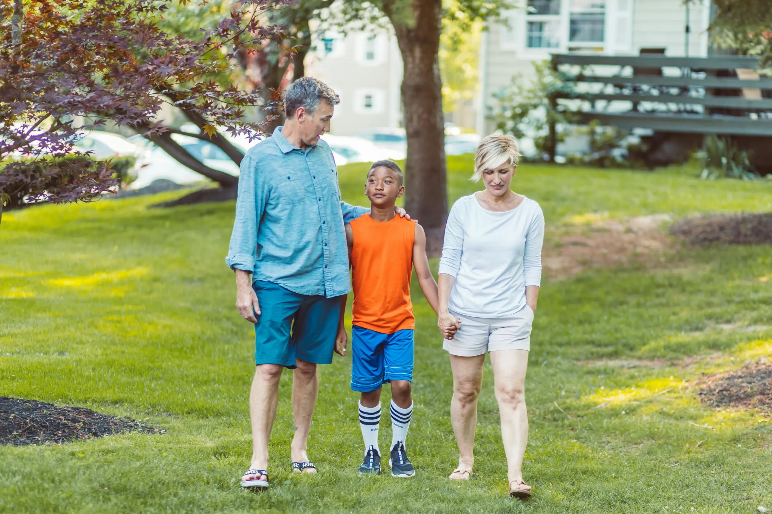 A young boy stands outside in the middle of his parents holding hands with them.