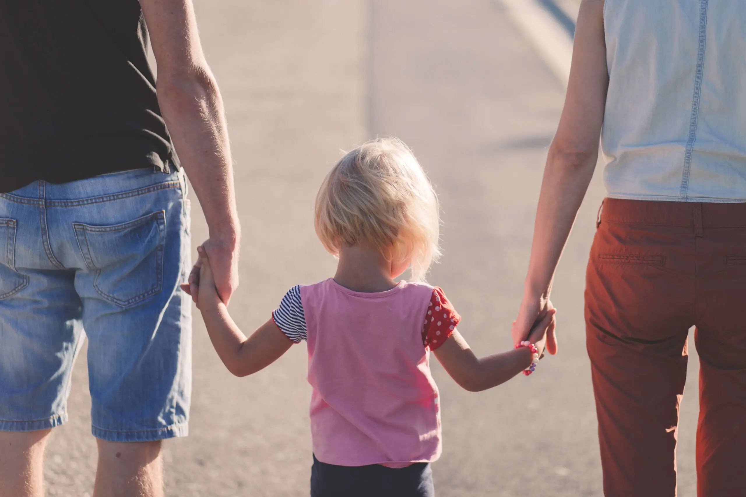 two parents holding their blonde female toddler's hands on a walk