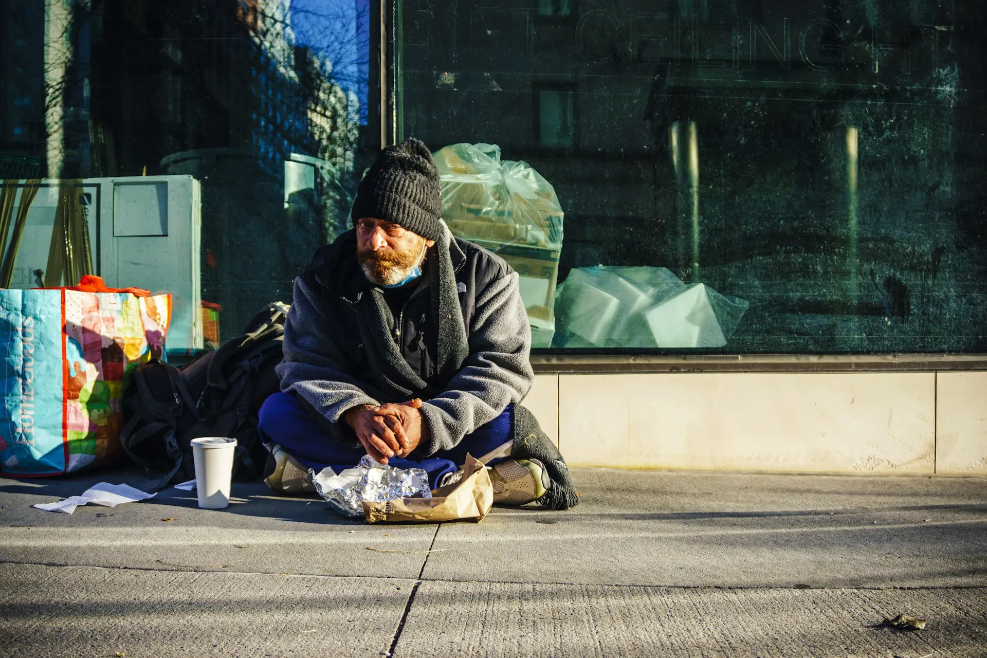 an unhoused man sits on the sidewalk