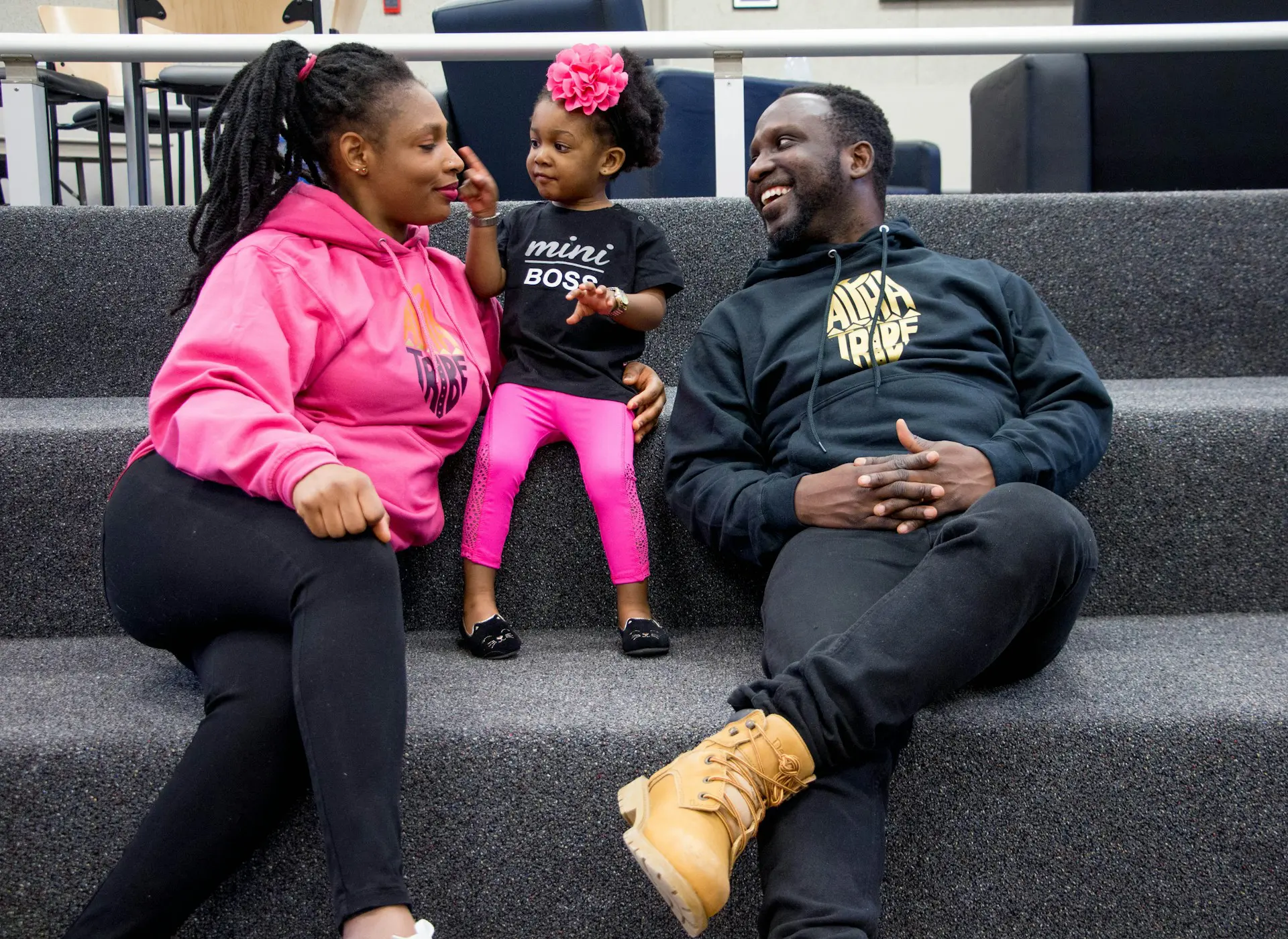 Black mother and father sit with their toddler daughter in a pink bow