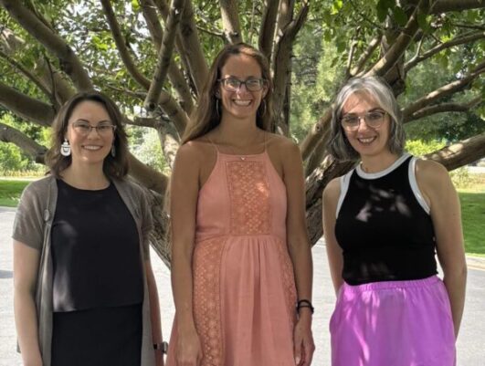 three women pose for a photo in front of a large tree